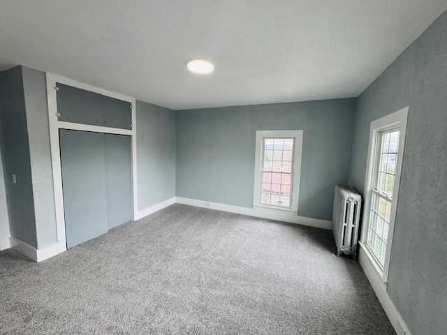 unfurnished bedroom with multiple windows, dark carpet, and radiator