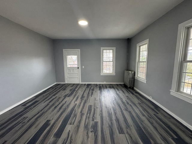 spare room featuring dark wood-style flooring, radiator, and baseboards