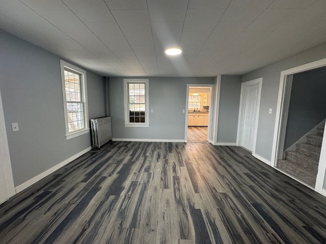 unfurnished room featuring radiator, stairs, baseboards, and dark wood-style flooring