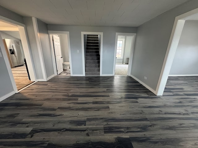 unfurnished bedroom with baseboards, wood finished floors, and stainless steel fridge with ice dispenser