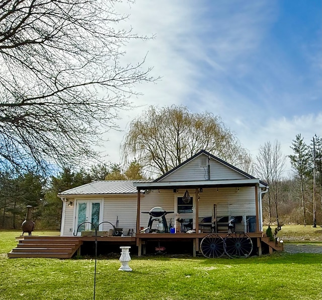 back of property with a wooden deck, a yard, french doors, and metal roof