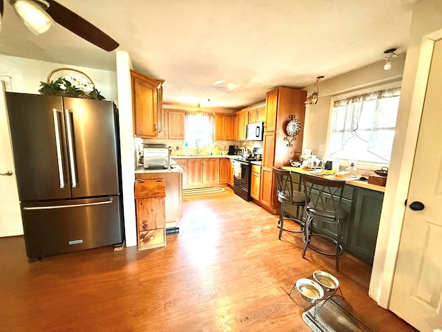 kitchen with light wood-style flooring, high quality fridge, black range with electric stovetop, ceiling fan, and light countertops