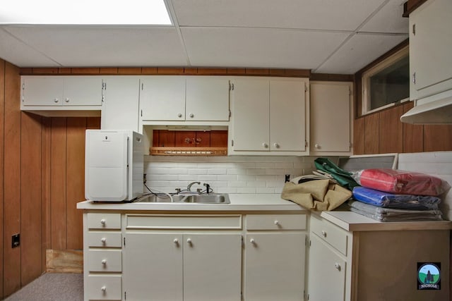 kitchen with sink, backsplash, wooden walls, a drop ceiling, and light colored carpet