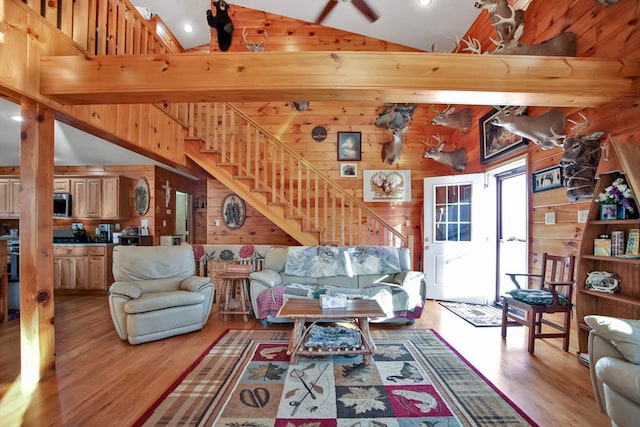 living area featuring stairs, high vaulted ceiling, wood walls, and wood finished floors