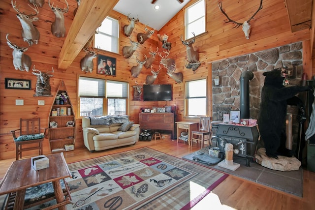 living room with a wood stove, wood walls, beamed ceiling, and wood finished floors