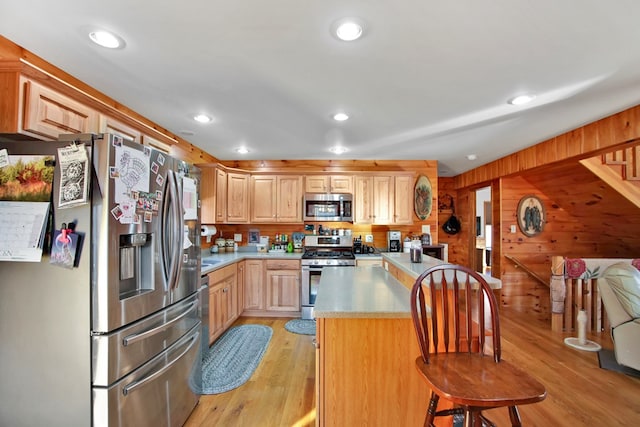 kitchen with a breakfast bar, wood walls, light countertops, appliances with stainless steel finishes, and light wood-type flooring