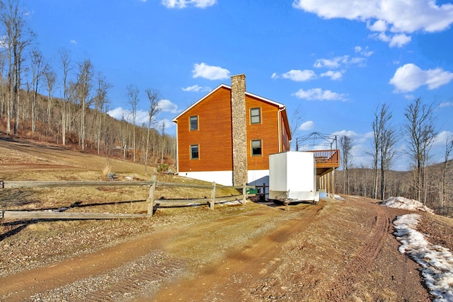 view of side of home with dirt driveway, a chimney, and fence