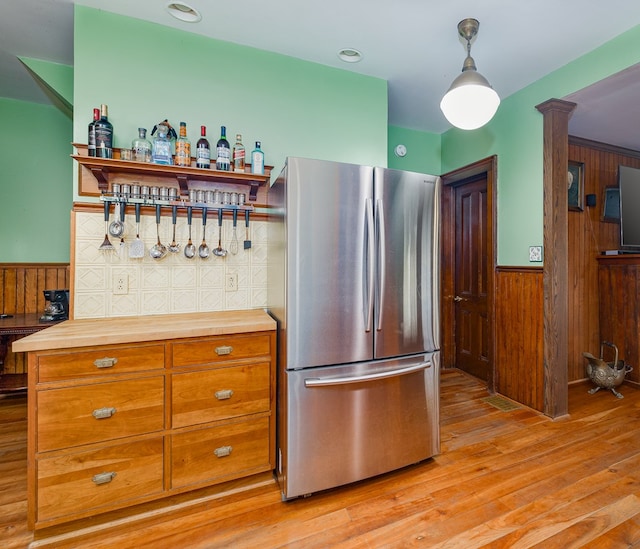 kitchen with wooden counters, decorative light fixtures, light hardwood / wood-style flooring, stainless steel refrigerator, and wood walls