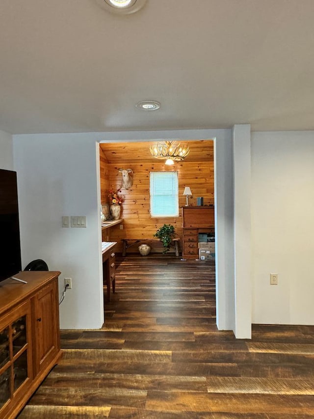 corridor featuring a notable chandelier, dark hardwood / wood-style floors, and wooden walls