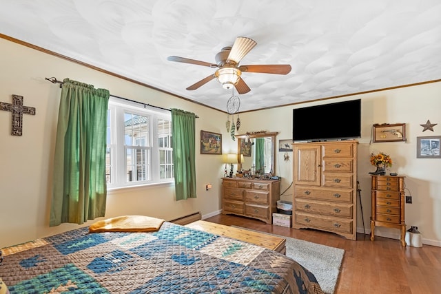 bedroom with a baseboard heating unit, crown molding, and wood finished floors