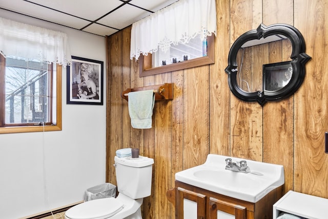 half bath with a paneled ceiling, toilet, a baseboard heating unit, wood walls, and vanity