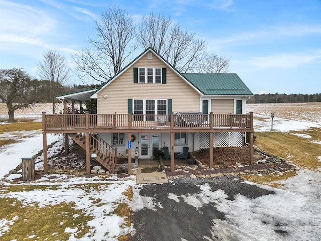 snow covered house with french doors, metal roof, a wooden deck, and stairs