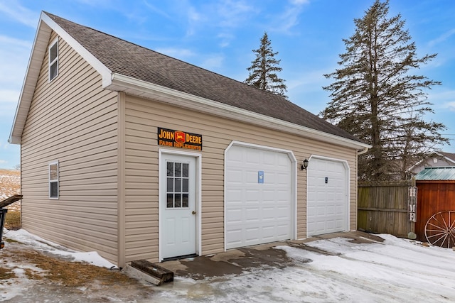 snow covered garage featuring fence