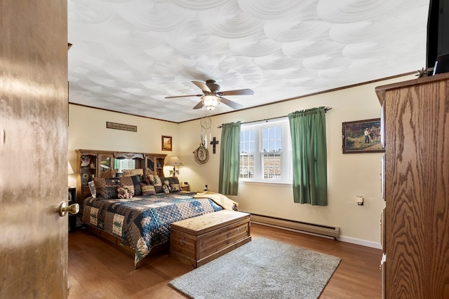 bedroom featuring baseboard heating, ornamental molding, ceiling fan, wood finished floors, and baseboards