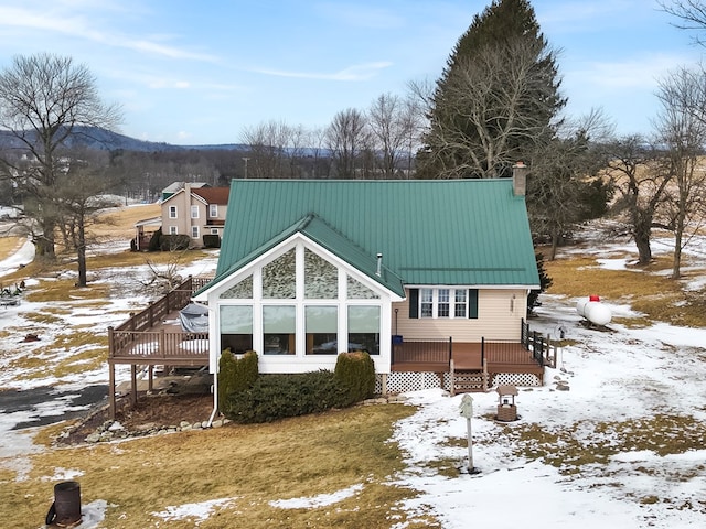 snow covered rear of property with a chimney, metal roof, and a deck