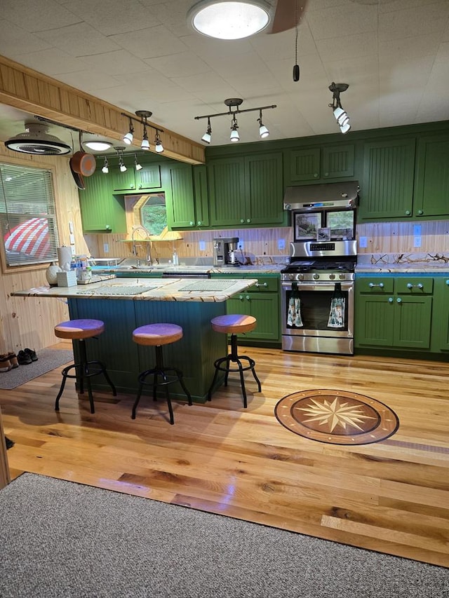 kitchen featuring a breakfast bar, backsplash, stainless steel range with gas stovetop, light hardwood / wood-style floors, and green cabinetry