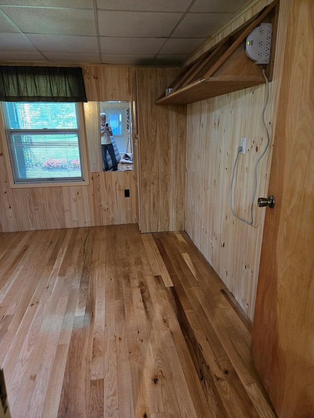 interior space featuring a paneled ceiling, light hardwood / wood-style floors, and wood walls