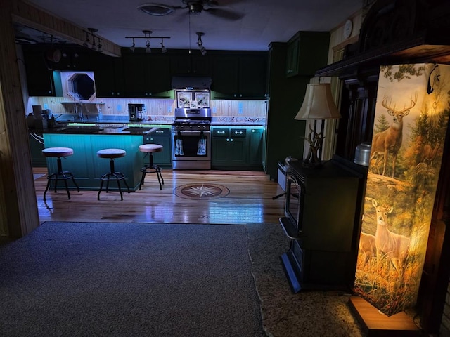 kitchen featuring a kitchen bar, exhaust hood, ceiling fan, gas range, and light wood-type flooring