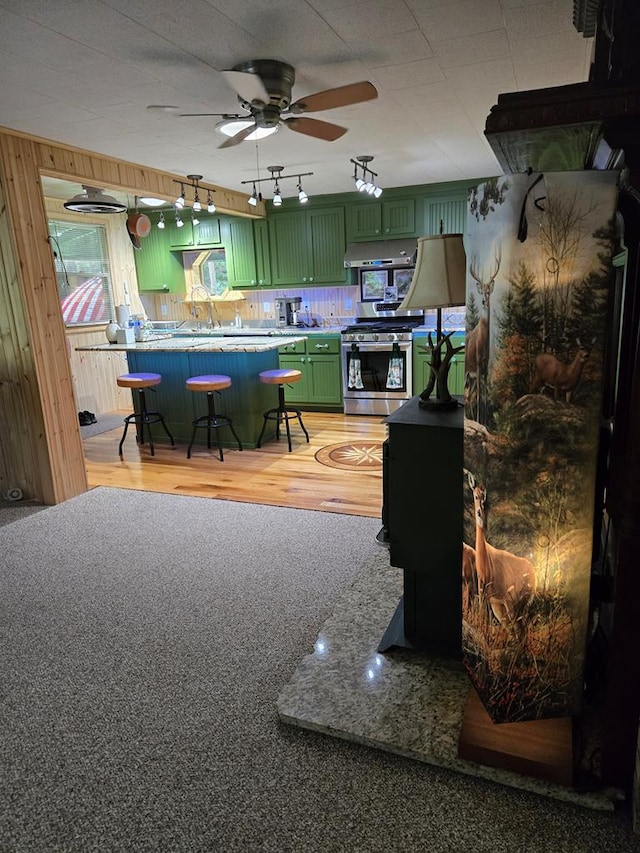 kitchen featuring a breakfast bar area, ceiling fan, green cabinetry, gas range, and wood walls