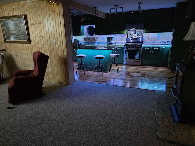 kitchen with hardwood / wood-style flooring, stainless steel gas range, a breakfast bar, wooden walls, and extractor fan