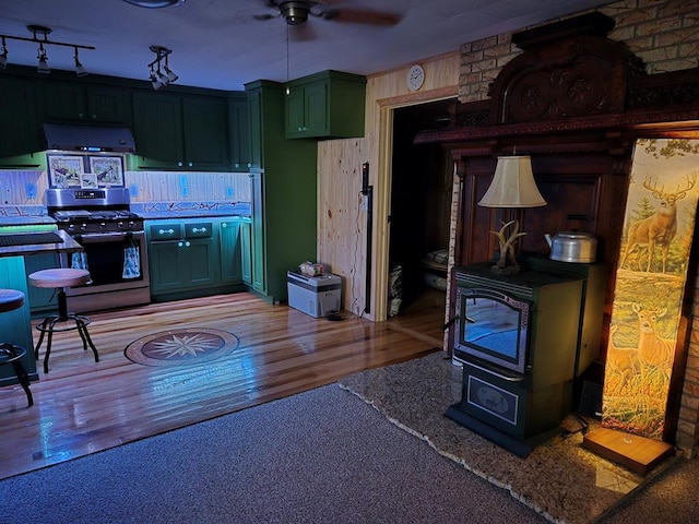 kitchen featuring ceiling fan, stainless steel gas range, light wood-type flooring, and a wood stove