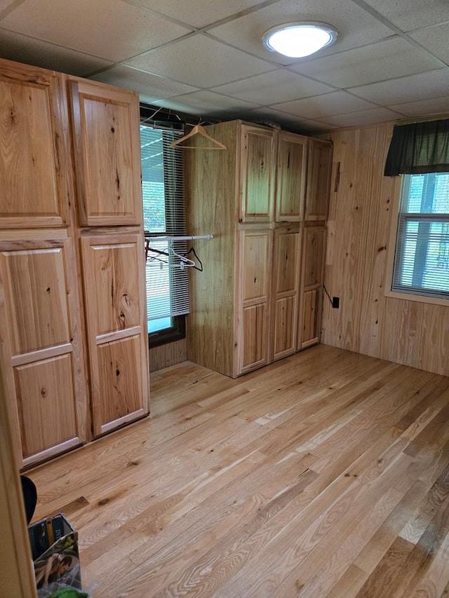 unfurnished bedroom with a paneled ceiling, wood walls, and light wood-type flooring