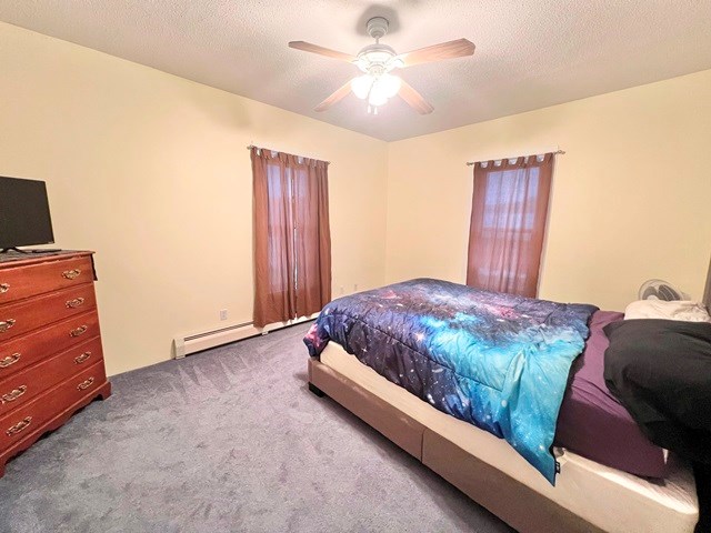 carpeted bedroom with a ceiling fan, a baseboard heating unit, and a textured ceiling