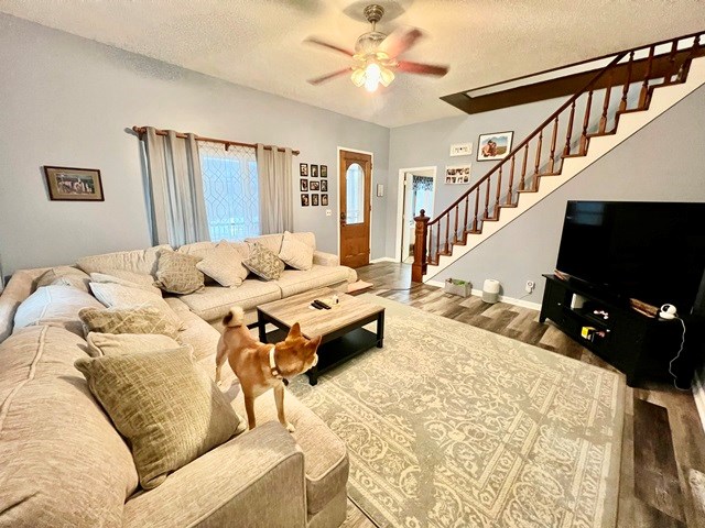 living room with a textured ceiling, stairway, wood finished floors, and a ceiling fan