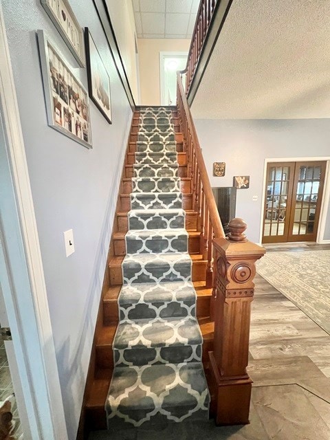 stairs with french doors, a drop ceiling, a textured ceiling, and wood finished floors