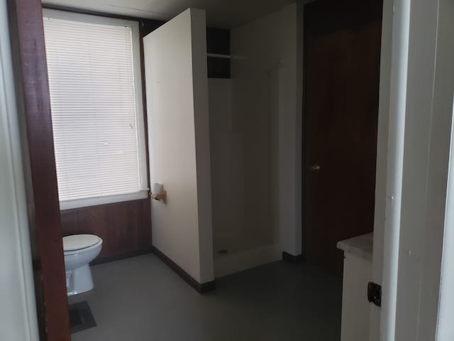 bathroom featuring wooden walls, toilet, a shower, and vanity