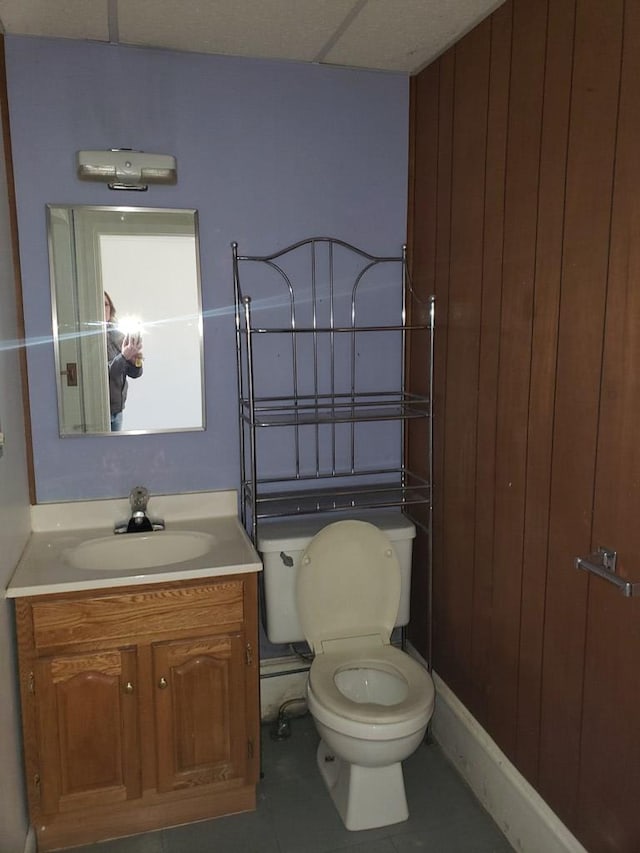 bathroom featuring tile patterned floors, wooden walls, vanity, and toilet