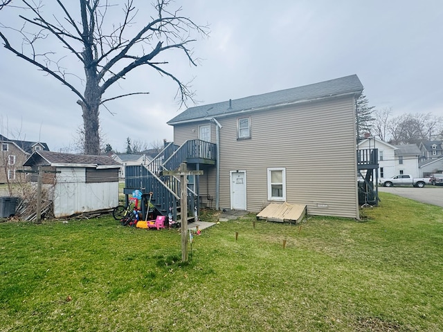 rear view of property with a yard, an outdoor structure, a storage unit, stairs, and central AC unit