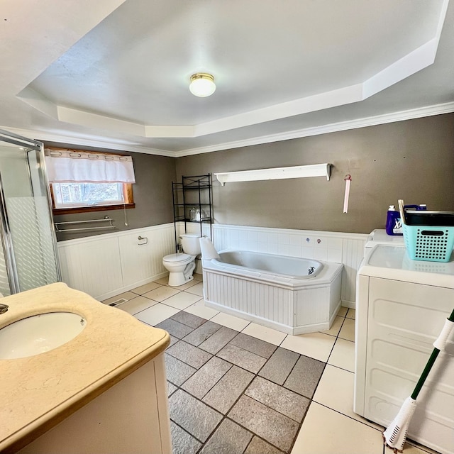 bathroom featuring washing machine and dryer, vanity, a tub to relax in, toilet, and a raised ceiling