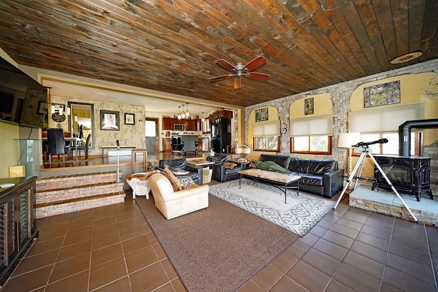 living room featuring ceiling fan, dark tile patterned floors, a wood stove, and wooden ceiling