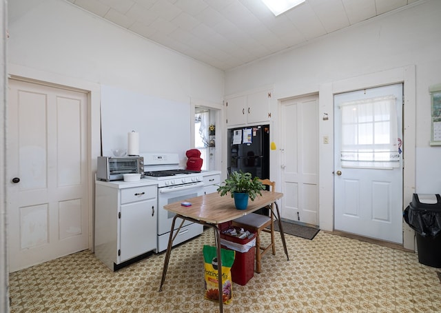 kitchen with white range with gas stovetop, white cabinetry, and black fridge