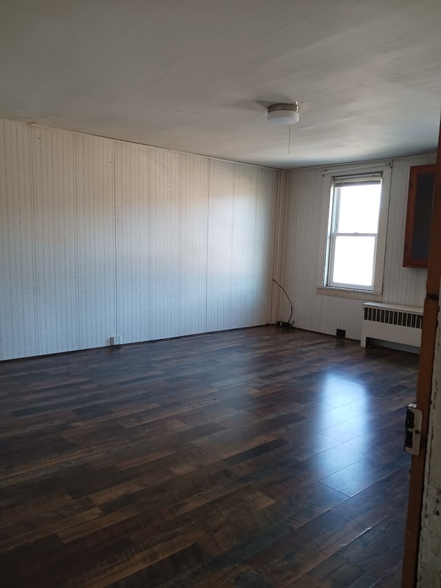 empty room with dark hardwood / wood-style flooring and radiator