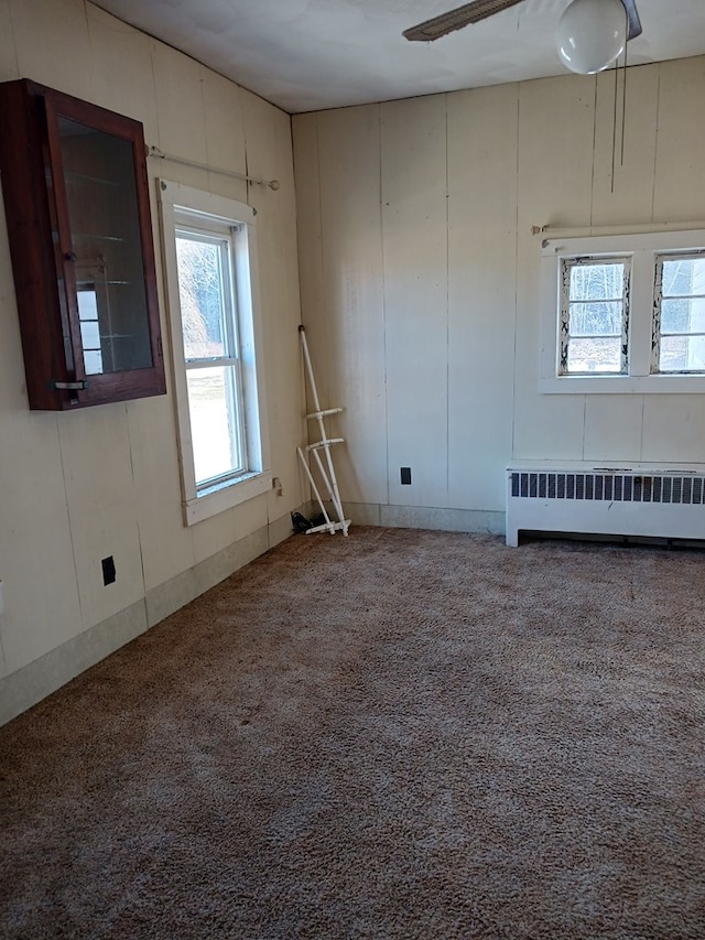 carpeted empty room featuring radiator heating unit and a healthy amount of sunlight