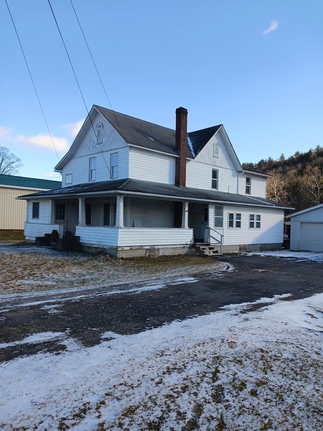 snow covered rear of property with a garage and covered porch