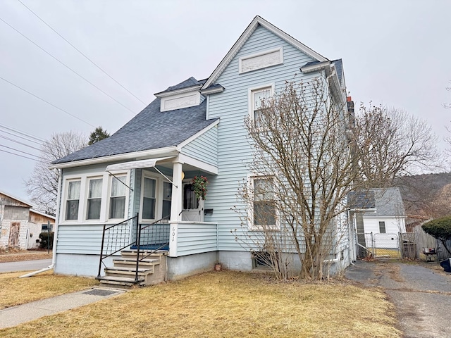 view of front of house featuring a porch, fence, roof with shingles, a gate, and a front yard