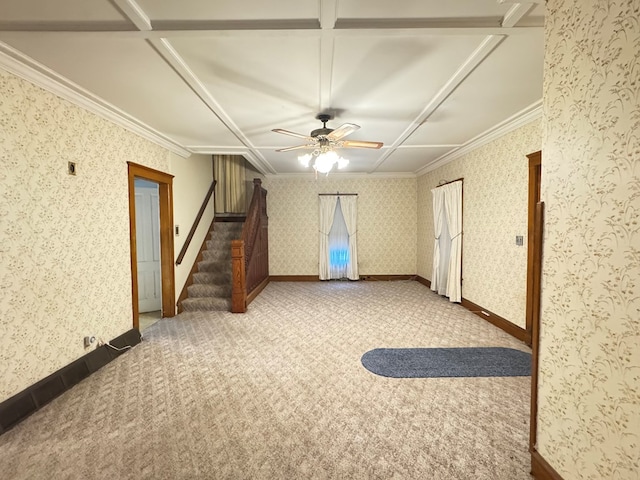 carpeted empty room with wallpapered walls, baseboards, a ceiling fan, ornamental molding, and stairs