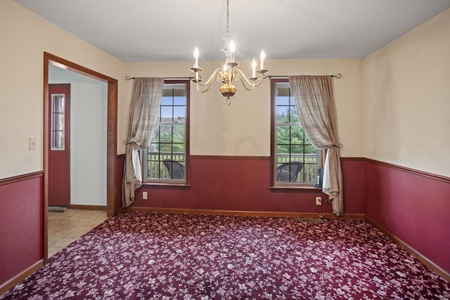 carpeted empty room featuring a chandelier and baseboards