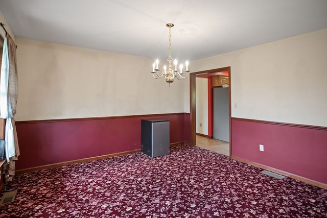 empty room featuring a chandelier, visible vents, carpet, and baseboards