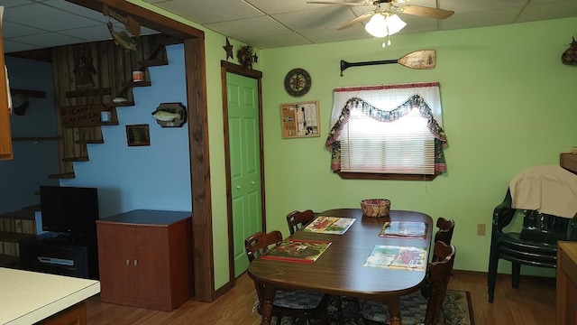 dining area featuring ceiling fan, a drop ceiling, and wood-type flooring