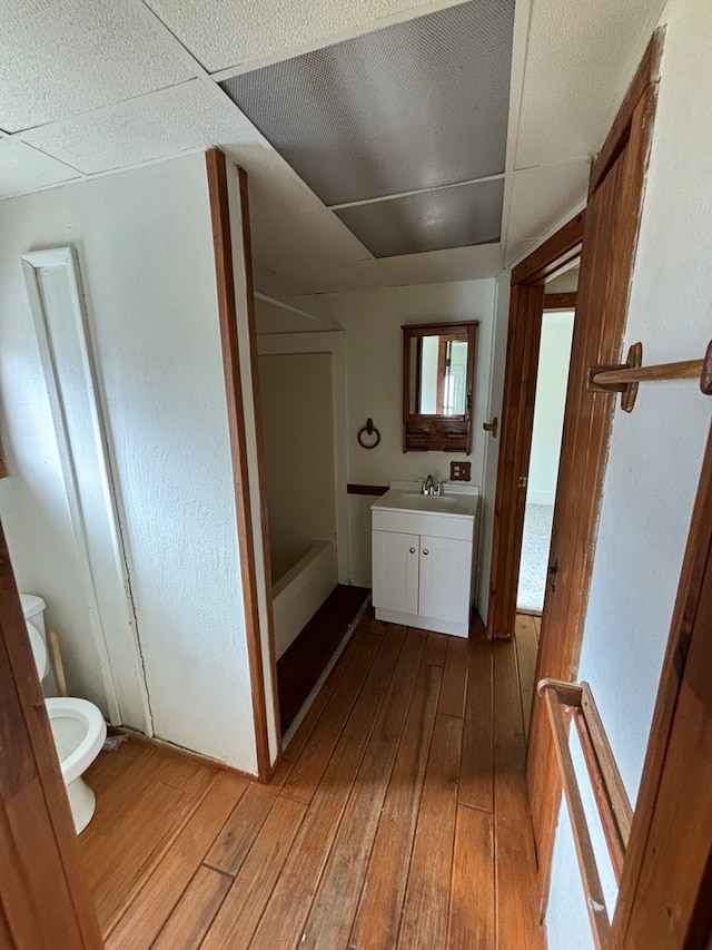 bathroom featuring hardwood / wood-style floors, vanity, a drop ceiling, and toilet