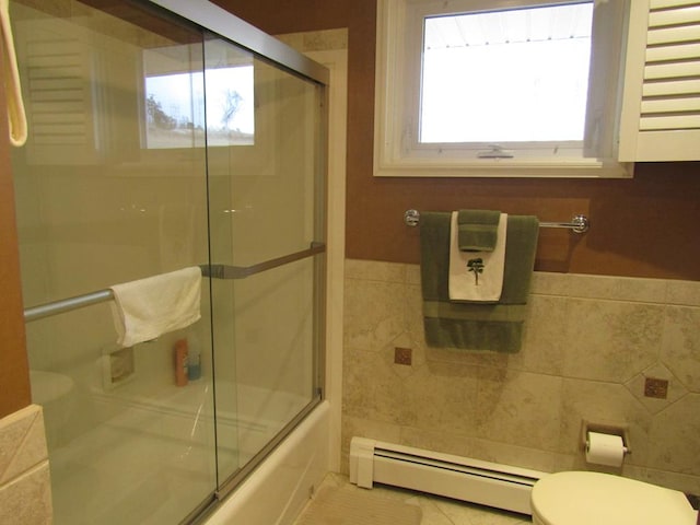 bathroom with tile walls, a baseboard heating unit, shower / bath combination with glass door, and toilet