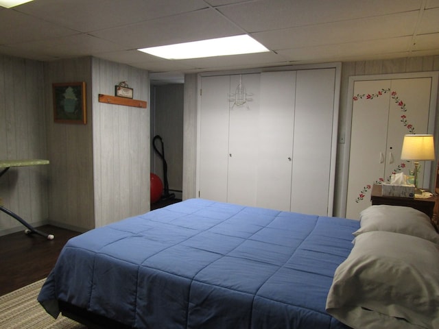 bedroom with dark hardwood / wood-style flooring, a baseboard heating unit, wood walls, and a drop ceiling