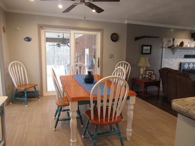 dining room featuring a brick fireplace, crown molding, ceiling fan, and light wood-type flooring