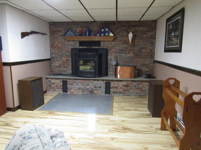 living room with a drop ceiling, wood-type flooring, and a wood stove