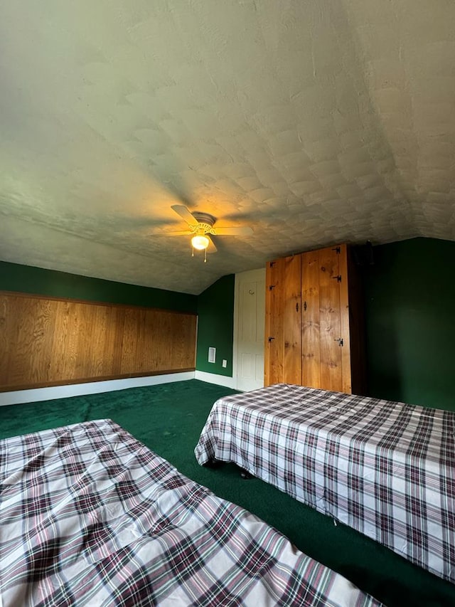 unfurnished bedroom featuring a textured ceiling, vaulted ceiling, ceiling fan, dark colored carpet, and wood walls