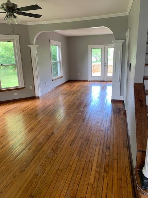 unfurnished living room featuring hardwood / wood-style floors, french doors, ceiling fan, ornamental molding, and decorative columns